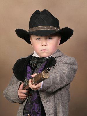 Ryan dressed as a cowboy, with a surly look on his face and pointing a rifle at the camera.