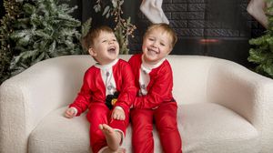 Owen and Ryan in Christmas jammies giggling on a white couch.